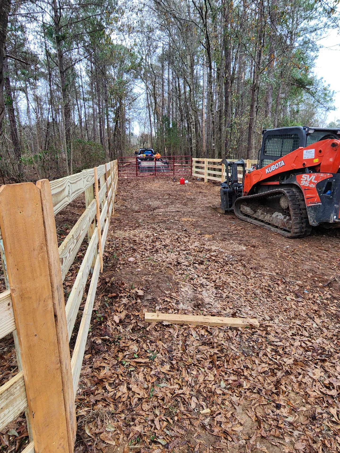 Bravo Fence crew installing a real wood farm fence and red gate with a Kubota loader in Alabama